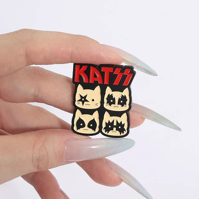 A black and cream enamel pin featuring four rock band cats with kiss makeup and a red kiss logo backpack lapel badge