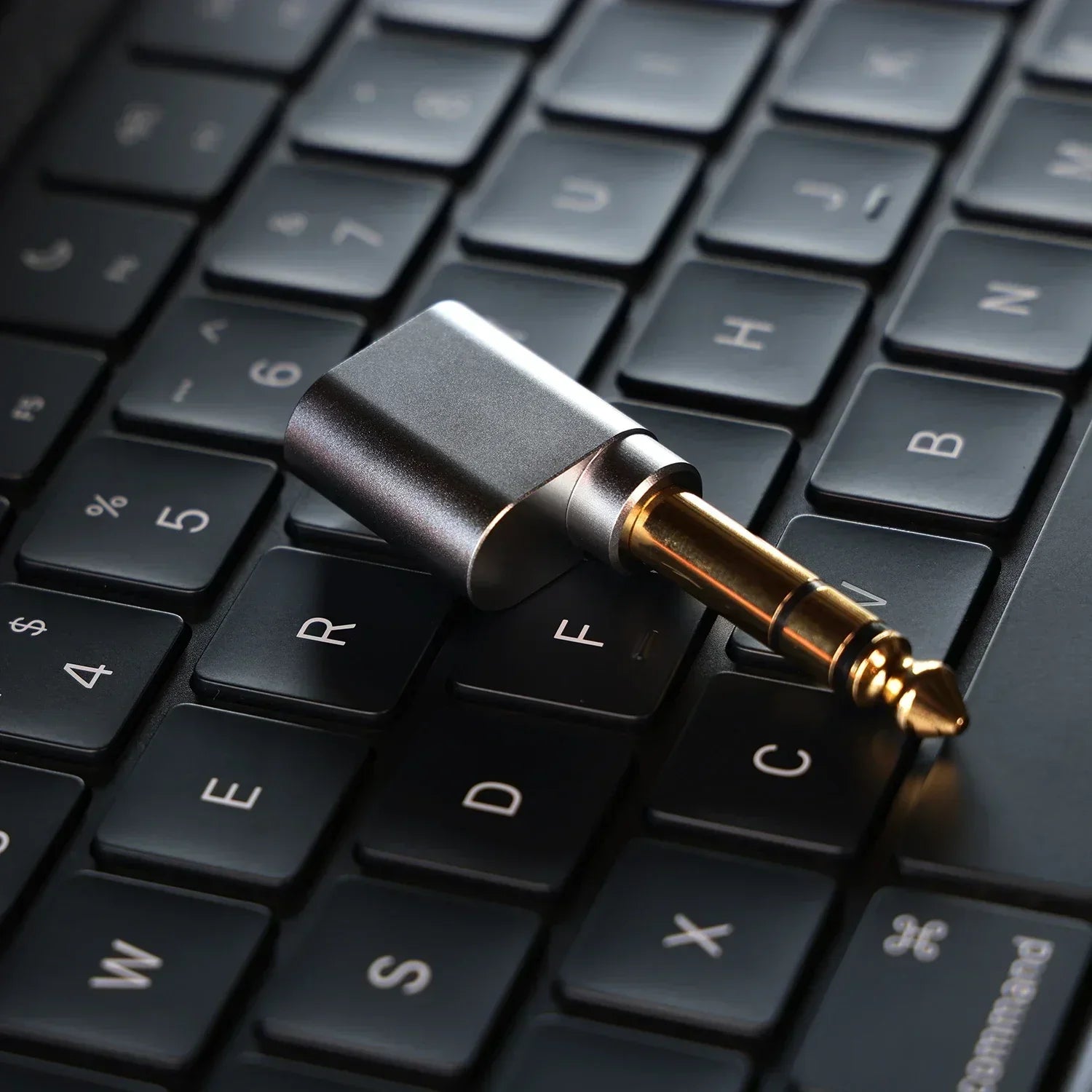 A sleek black and gold ddHiFi DJ65B 3.5mm audio adapter with matte finish on dark keyboard showing 35mm output port