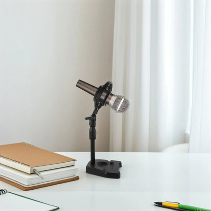 A sleek metallic condenser microphone with silver mesh grille on a black desktop microphone stand for live recording shockproof use