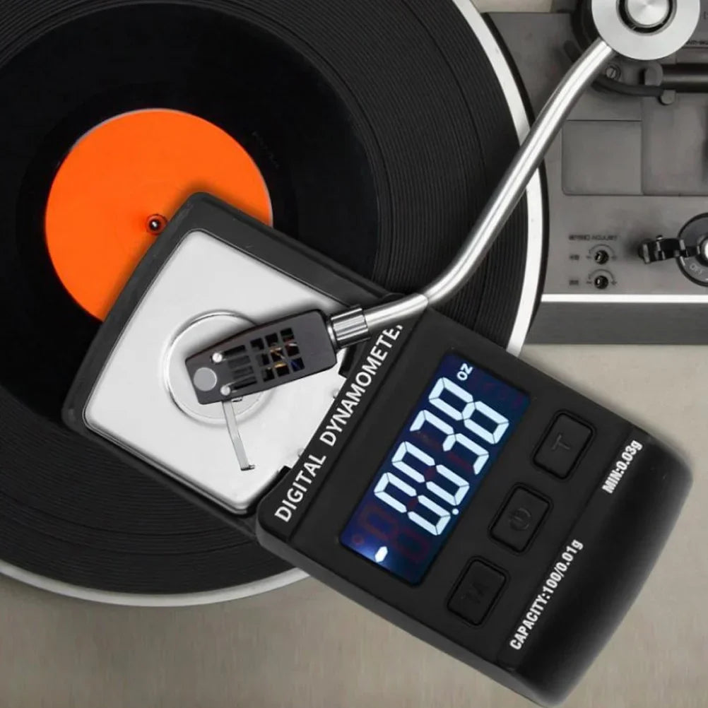 Black digital stylus force scale with silver stylus and blue backlight resting on orange vinyl record for needle pressure testing