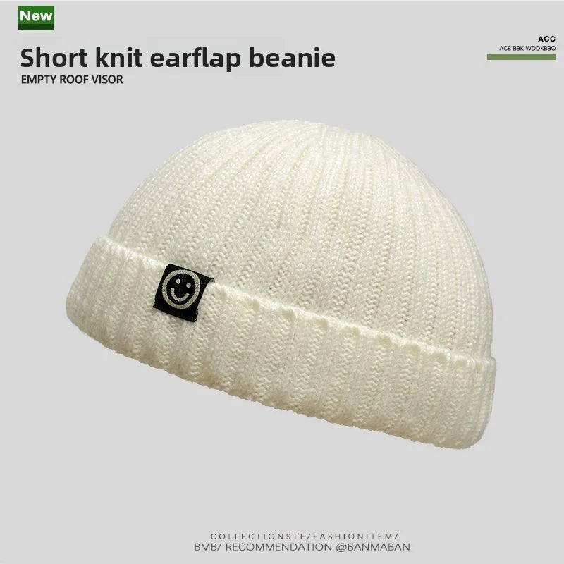 Cream-colored hip hop beanie with ribbed knit texture and black smiley patch perfect as a skullcap women winter hat