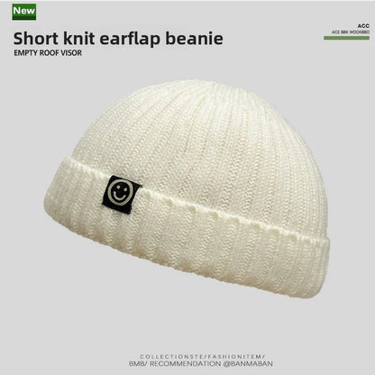 Cream-colored hip hop beanie with ribbed knit texture and black smiley patch perfect as a skullcap women winter hat