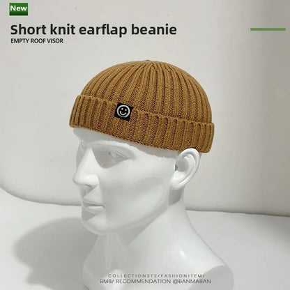 A tan short knit hip hop beanie with ribbed texture and black patch for men skullcap women winter warm brimless wear