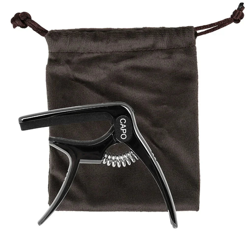Black metal galux universal guitar capo with silver spring change clamp key resting by dark brown drawstring pouch