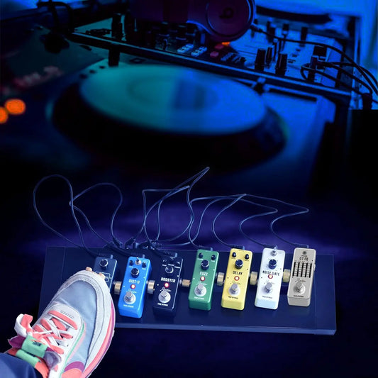 A row of colorful metal guitar effect pedals on a black footboard with daisy chain cables for 9v power adapters