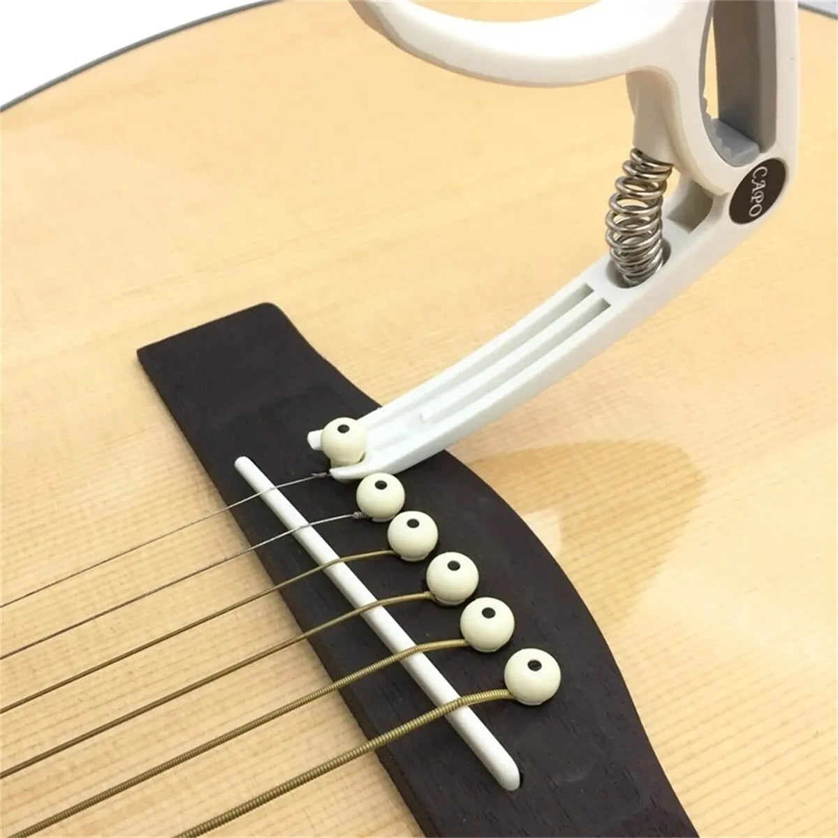 White plastic and metal guitar capo with spherical white knobs securing strings on acoustic classic guitar and ukulele