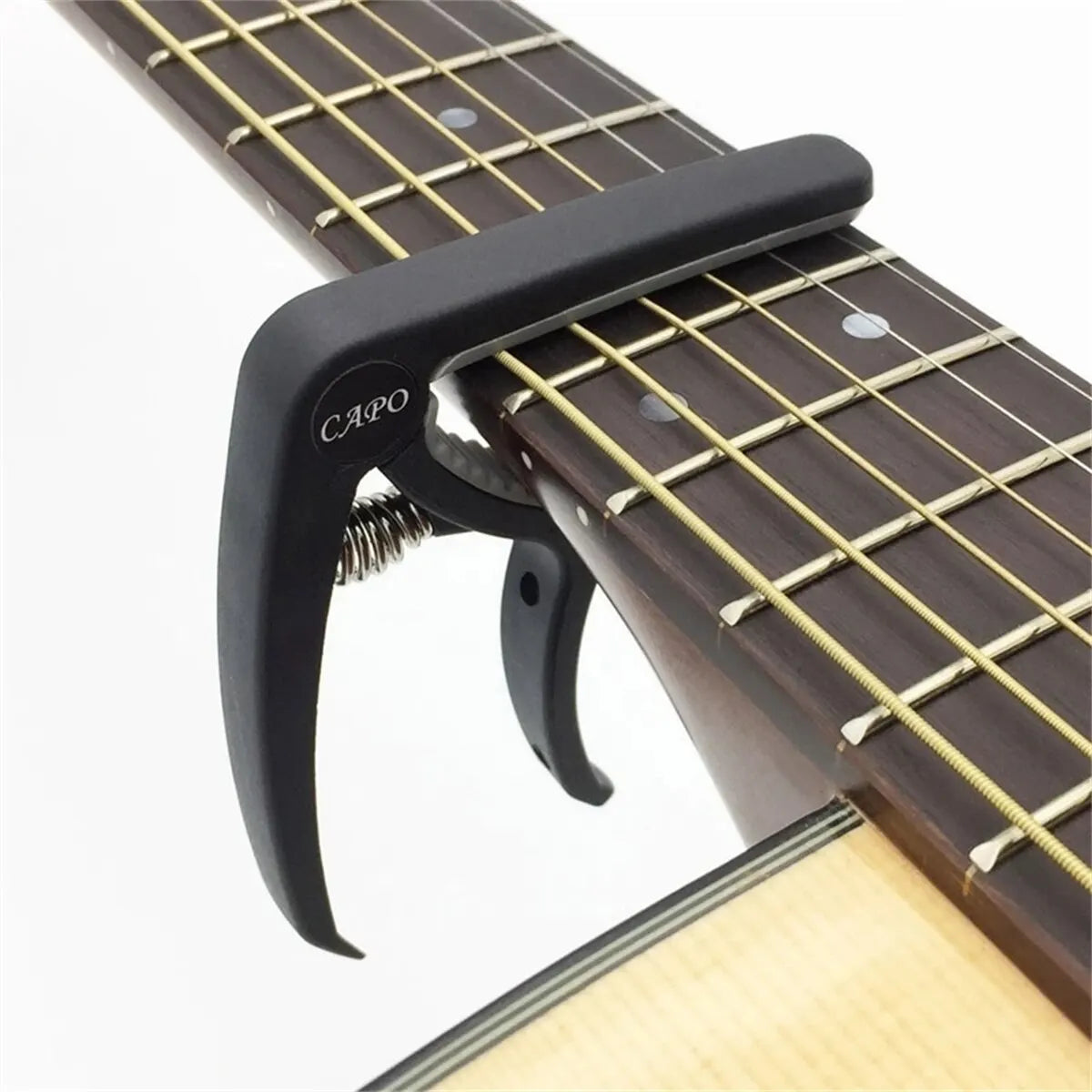 Black guitar capo with spring-loaded mechanism clamped on fretboard for acoustic classic guitar and musical instrument ukulele