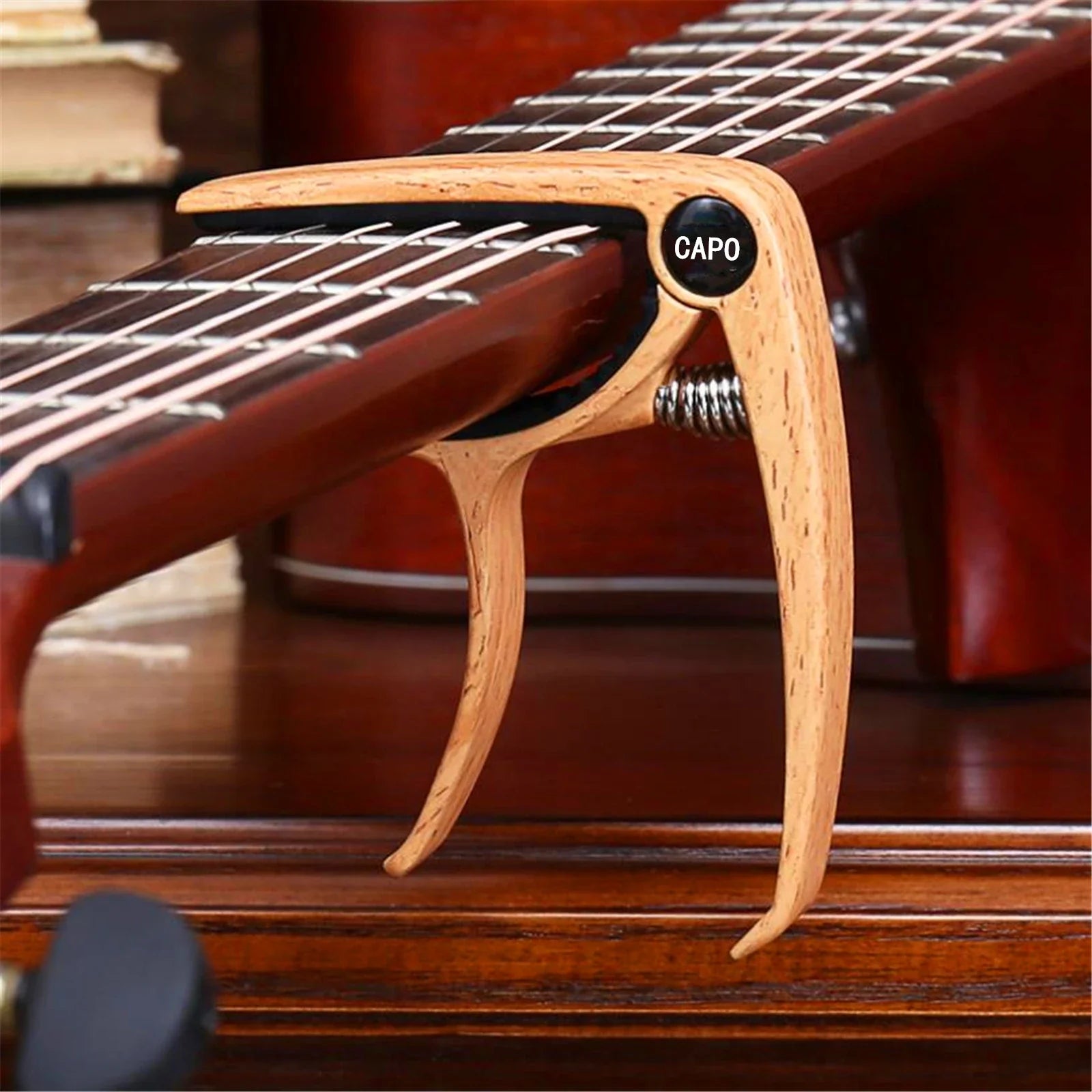 Light-colored wooden guitar capo metal with black capo label and visible metal spring for guitar tuner clamp use
