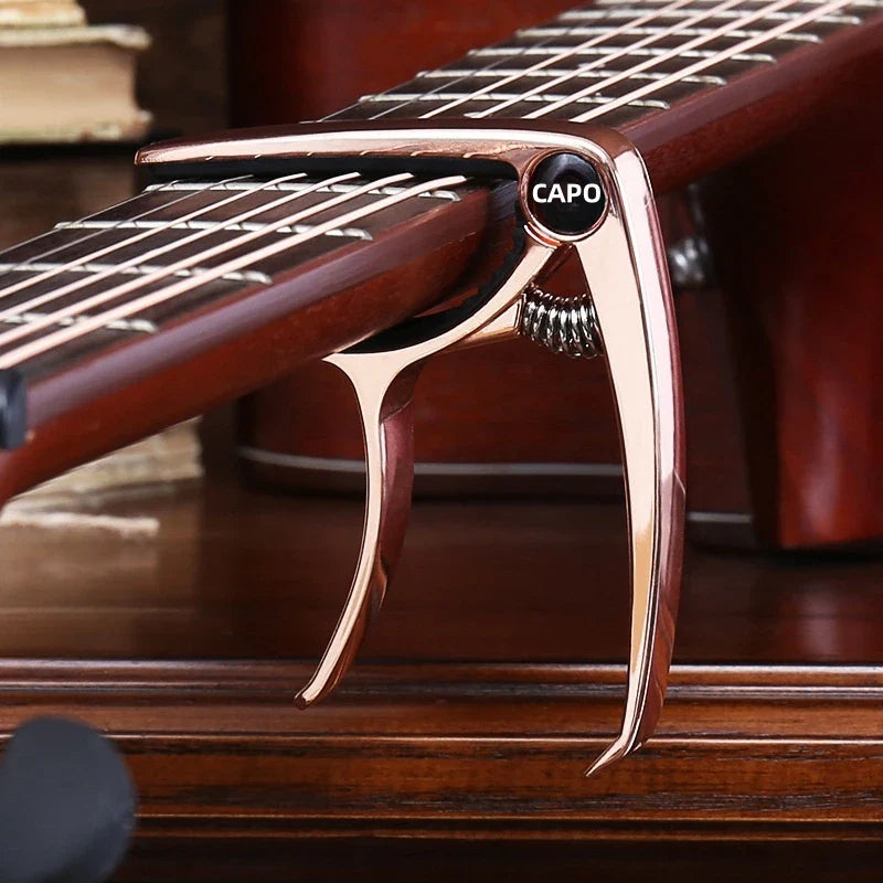 Rose gold guitar capo metal with black capo logo and spring mechanism made of zinc alloy construction for acoustic and electric guitars