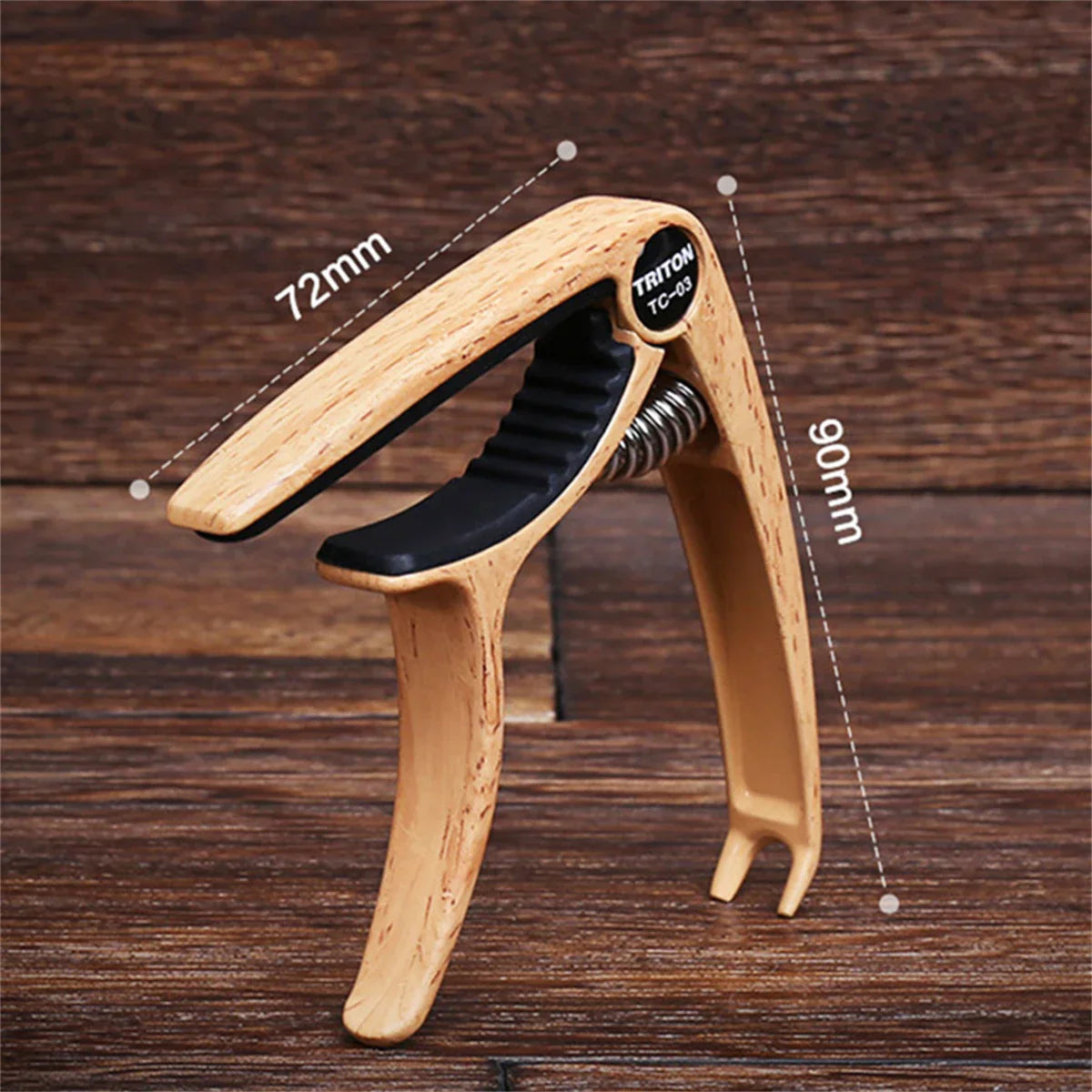 Light-colored wooden guitar capo metal with black rubber grip and visible spring featuring triton tc-03 brand zinc alloy construction