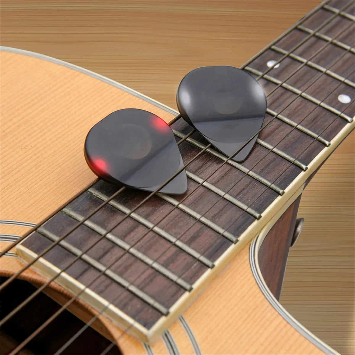 Two black glossy plastic guitar picks with high-sensitivity led light resting on an acoustic guitar fretboard instrument glowing plectrum