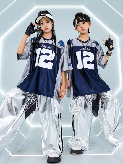 Two children wear hip hop girls matching navy blue oversized jerseys with white 12 and shiny metallic cargo pants for cool street dance