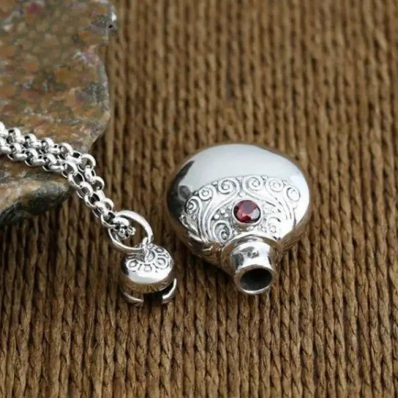 Silver ornamental money bag necklace pendant with intricate patterns and a red gemstone featuring shiny cubic zirconia accents