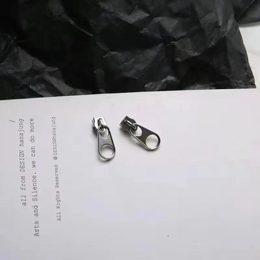 Two silver-toned metal hop zipper earrings with oval openings in vintage punk style punk style jewelry design