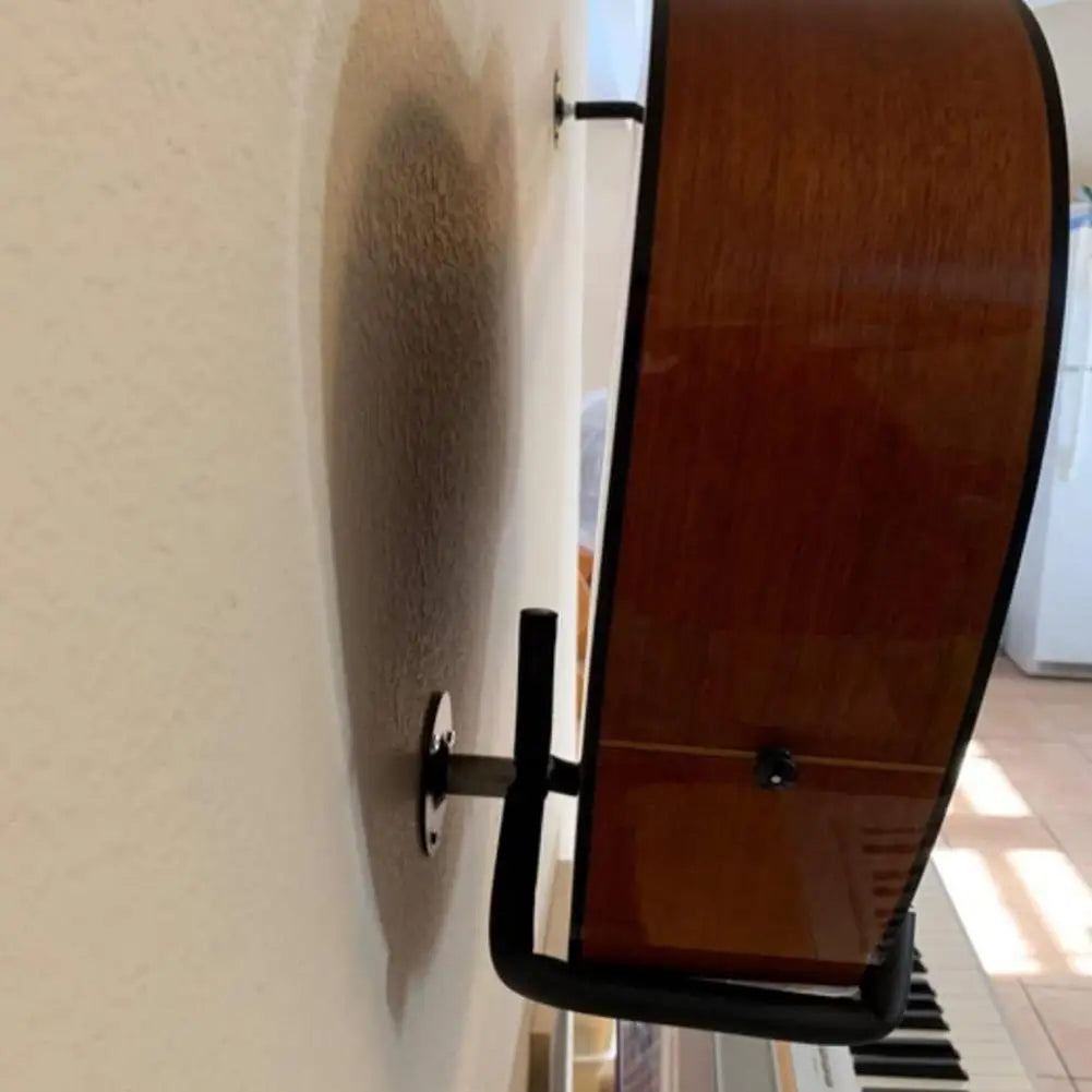 A polished wooden acoustic guitar with a glossy finish resting on a horizontal metal guitar wall mount hanger stand for acoustic guitar bass mandolins slat display