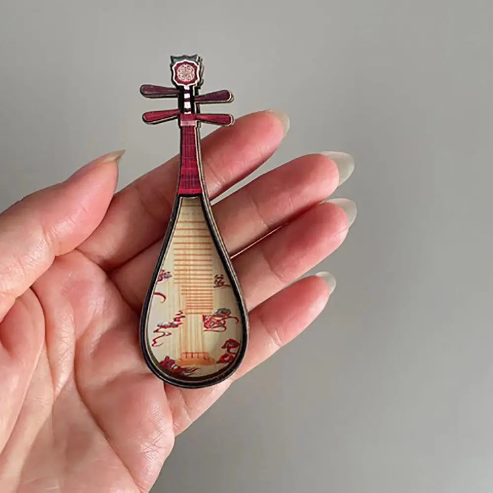 A delicate red and cream-colored lute-shaped dollhouse musical instrument with intricate floral courtesan pattern detailing
