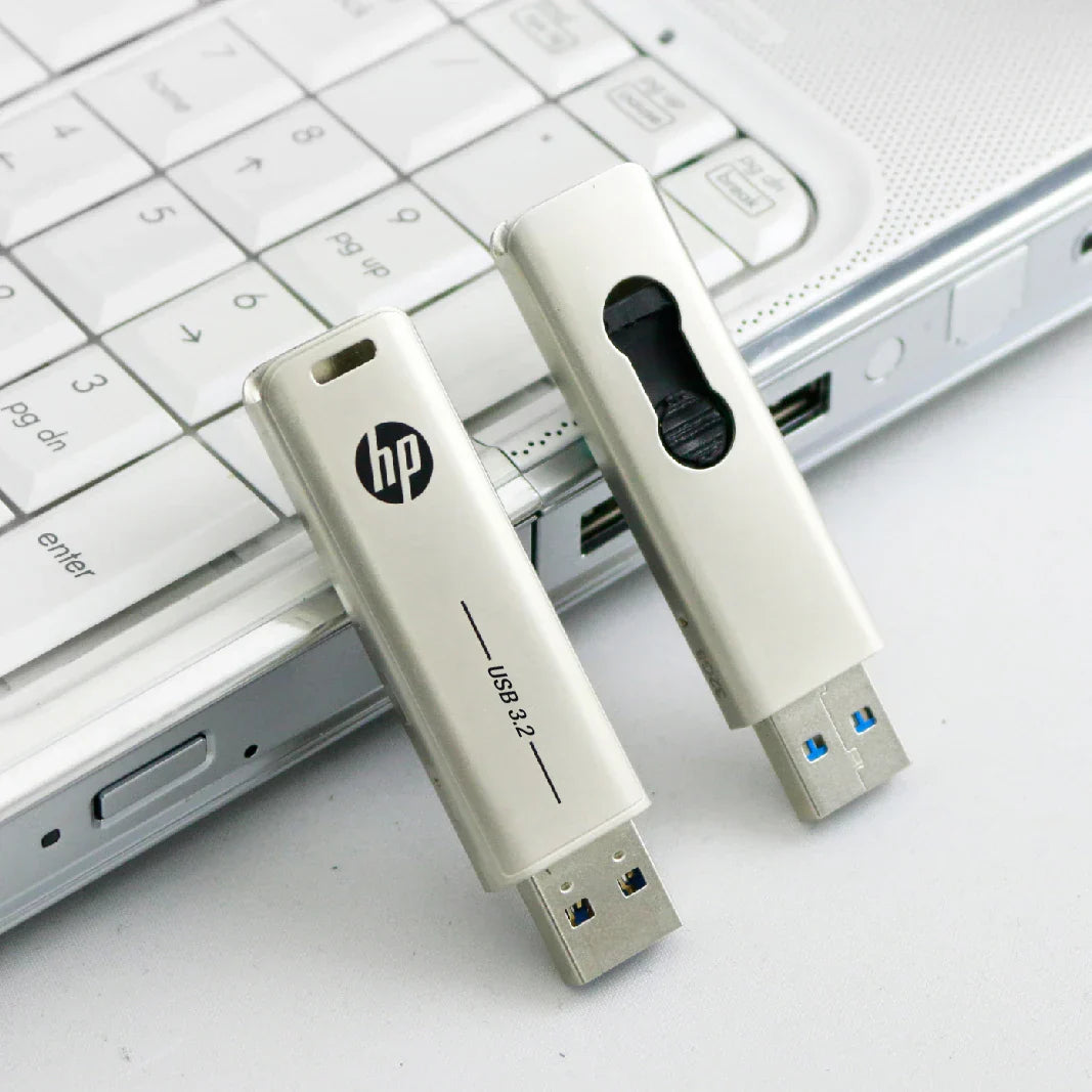 Two white HP metal USB 3.2 flash drives 32GB 64GB and pendrive 128GB 256GB on a silver laptop keyboard