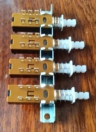 Four gold-colored interlock push button switch piano type dpdt with white knobs and metallic mounting brackets for electronics