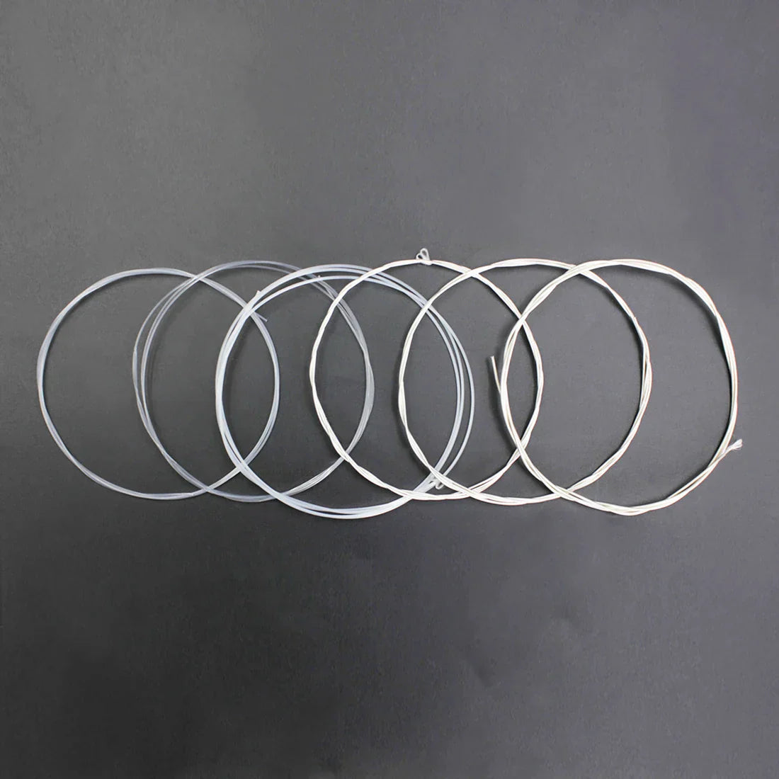 Six coiled white transparent nylon string loops for irin c670 classical guitar strings replacement parts on dark surface