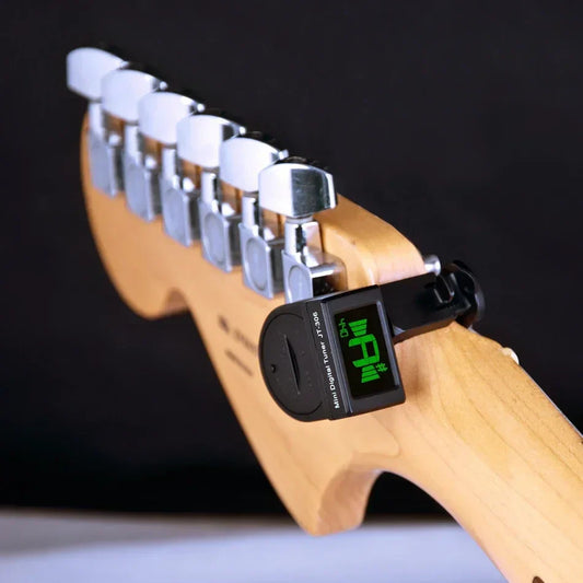 Black mini guitar tuner with green lcd display mounted on light wood fretboard for electric acoustic classic chromatic guitar bass