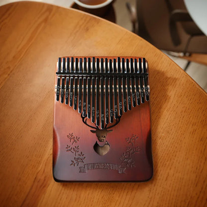 A reddish-brown full wood kalimba with 21 keys black metal tines an engraved deer head and instruction carrying bag