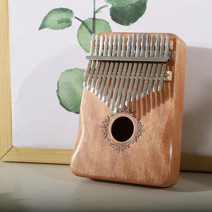 A light brown mahogany wood kalimba music instrument thumb piano with 17 silver metal tines and ornate circular design