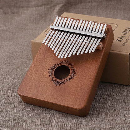 A wooden kalimba music instrument thumb piano with 17 silver tines and ornate circular design on mahogany finish