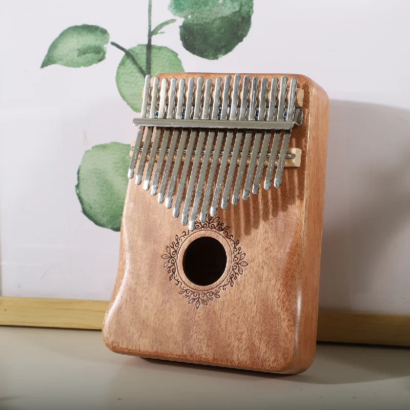 A light brown mahogany wood kalimba music instrument with 17 silver tines and ornate circular engraving thumb piano