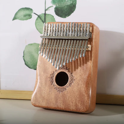 A light brown mahogany wood kalimba music instrument with 17 silver tines and ornate circular engraving thumb piano