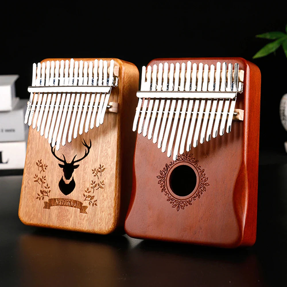 Two mahogany wood kalimba music instruments with 17 keys, one light with deer engraving, one reddish with ornate design thumb pianos
