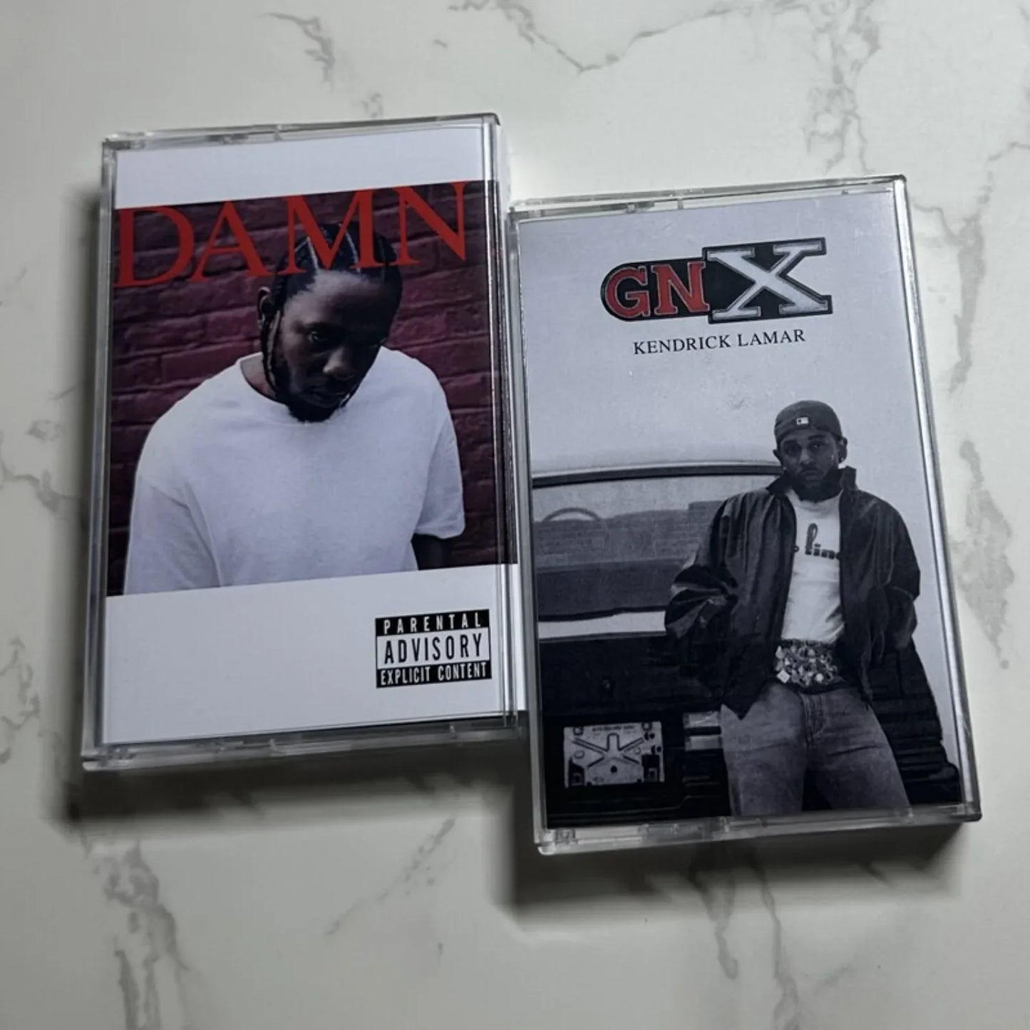 Two transparent plastic hip hop rap cassette tapes featuring kendrick lamar’s damn and gnx albums with distinct cover art