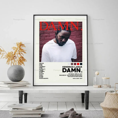 Black-framed kendrick lamar damn album cover poster with bold red lettering and white t-shirt on brick wall background