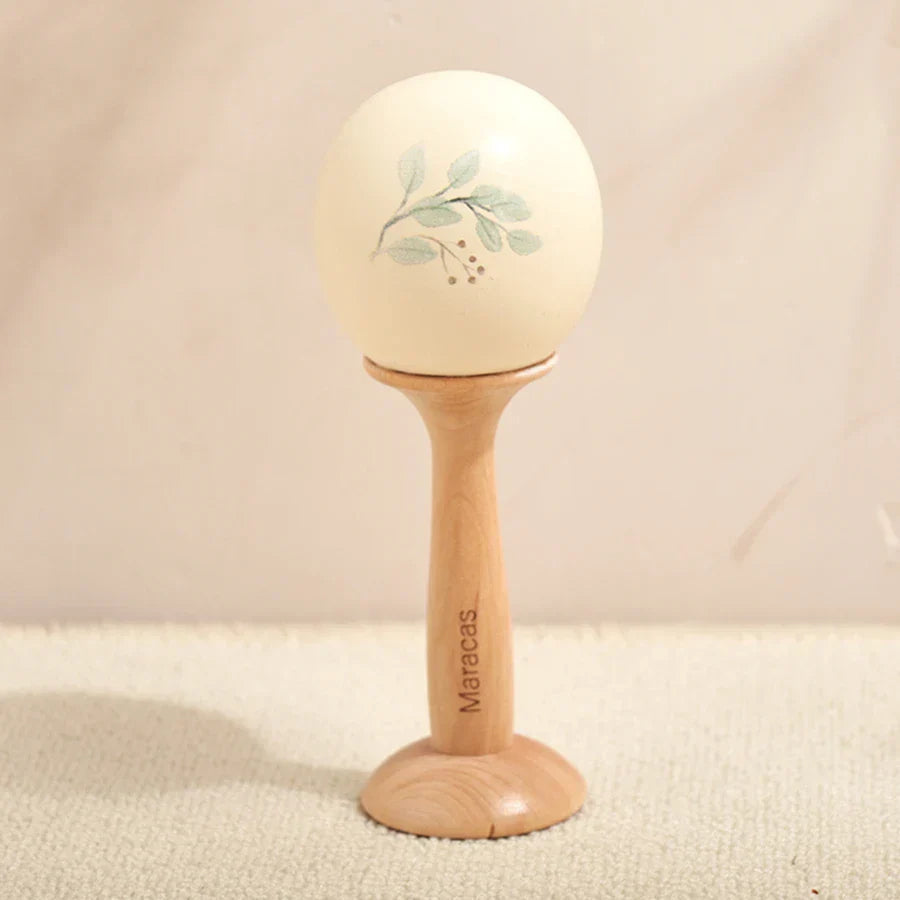 Cream-colored ceramic maraca with hand-painted green leaf design on light wood stand for kids wooden montessori toys musical use