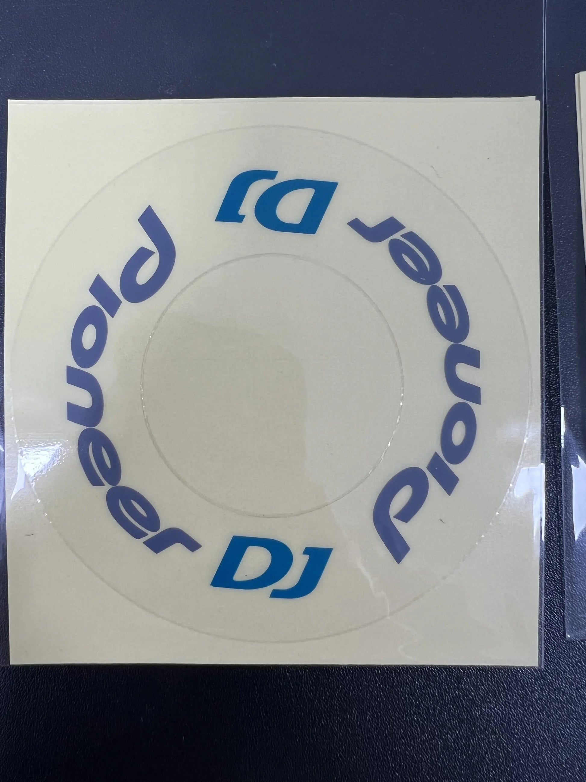 A circular transparent pioneer dj protective film cdj sticker with blue lettering on beige backing for large turntable