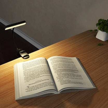 A sleek black led music stand light with a flexible gooseneck and rechargeable clip featuring stepless dimming illuminating an open book on wood