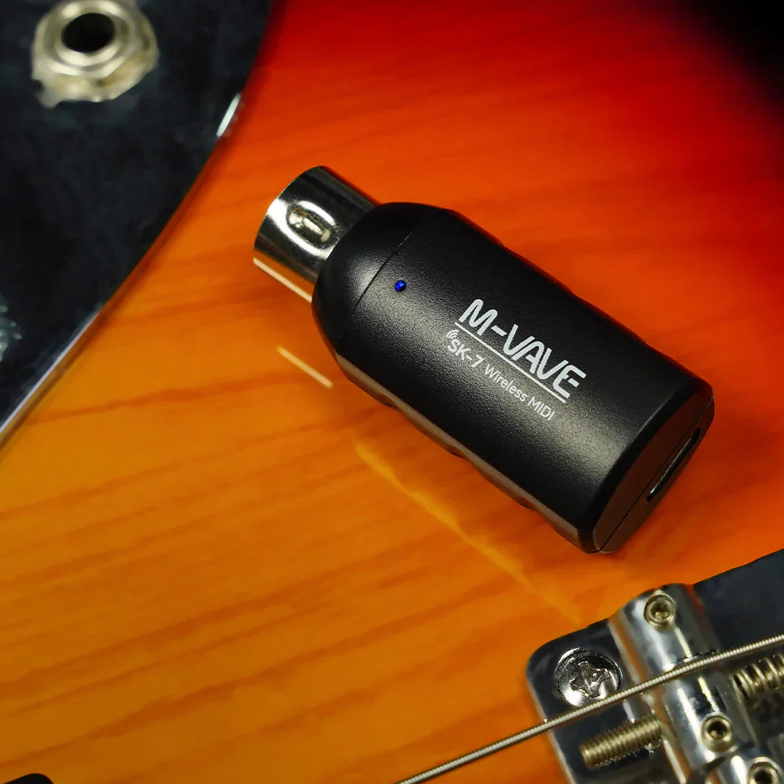 Black m-vave sk7 midi adapter wireless midi receiver with metallic connector and blue led indicator on orange guitar body