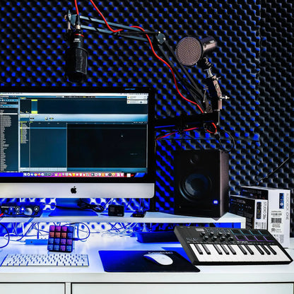Black studio microphone mounted on red and black articulated arm next to midi keyboard controller with backlit drum pads