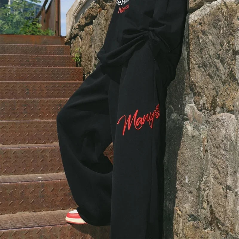 Black printed wide leg pants with red embroidered manys branding for men’s y2k streetwear baggy hip hop fashion