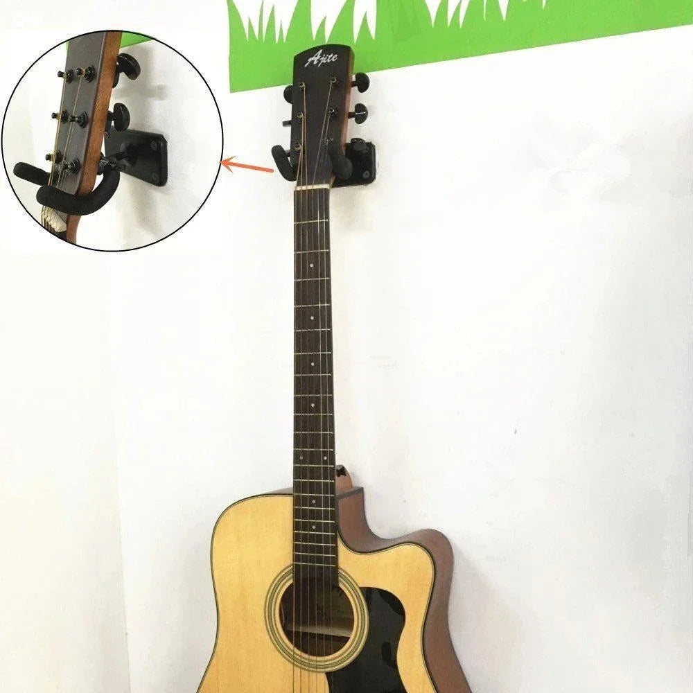 A light wood acoustic guitar with black pickguard on a black arite metal guitar hanger hook wall mount for ukulele violin bass