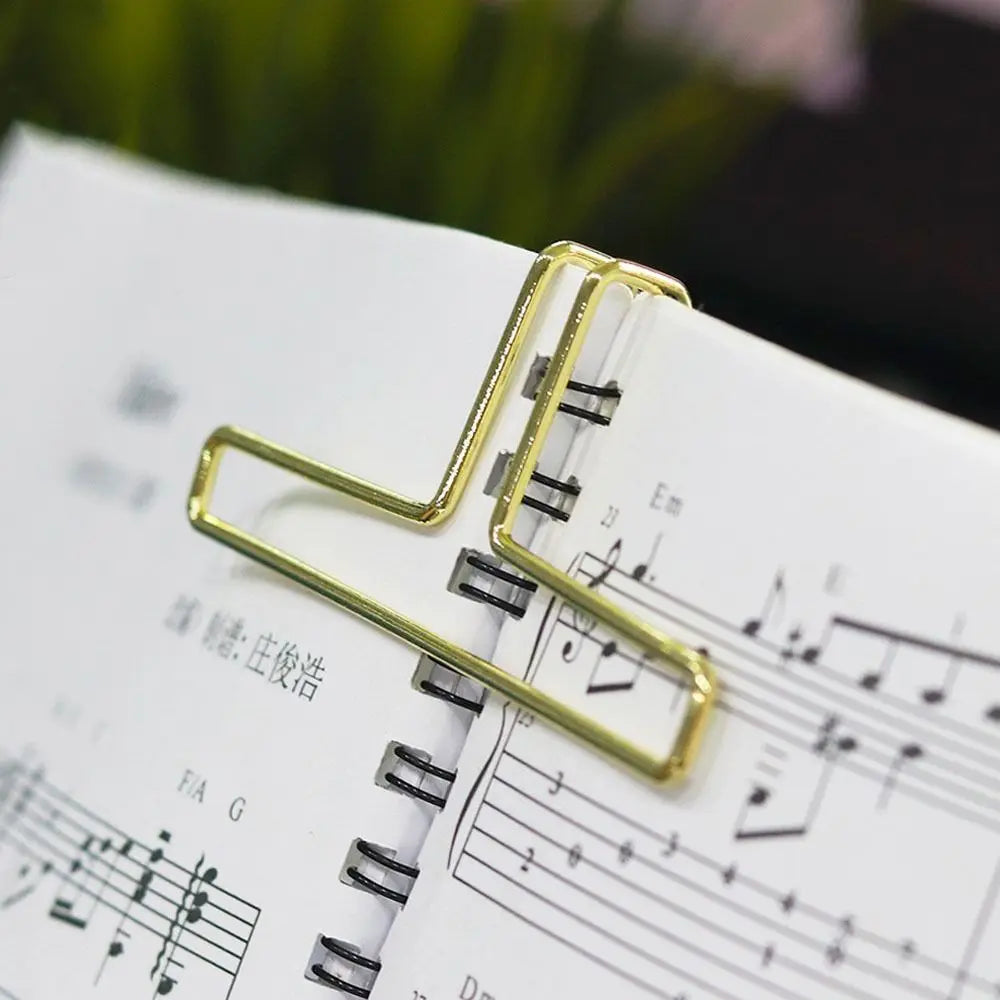 Gold-colored metal music book clip holding open spiral-bound score as page holder for pianos and cooking recipe magazines