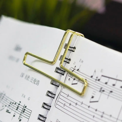 Gold-colored metal music book clip holding open spiral-bound score as page holder for pianos and cooking recipe magazines