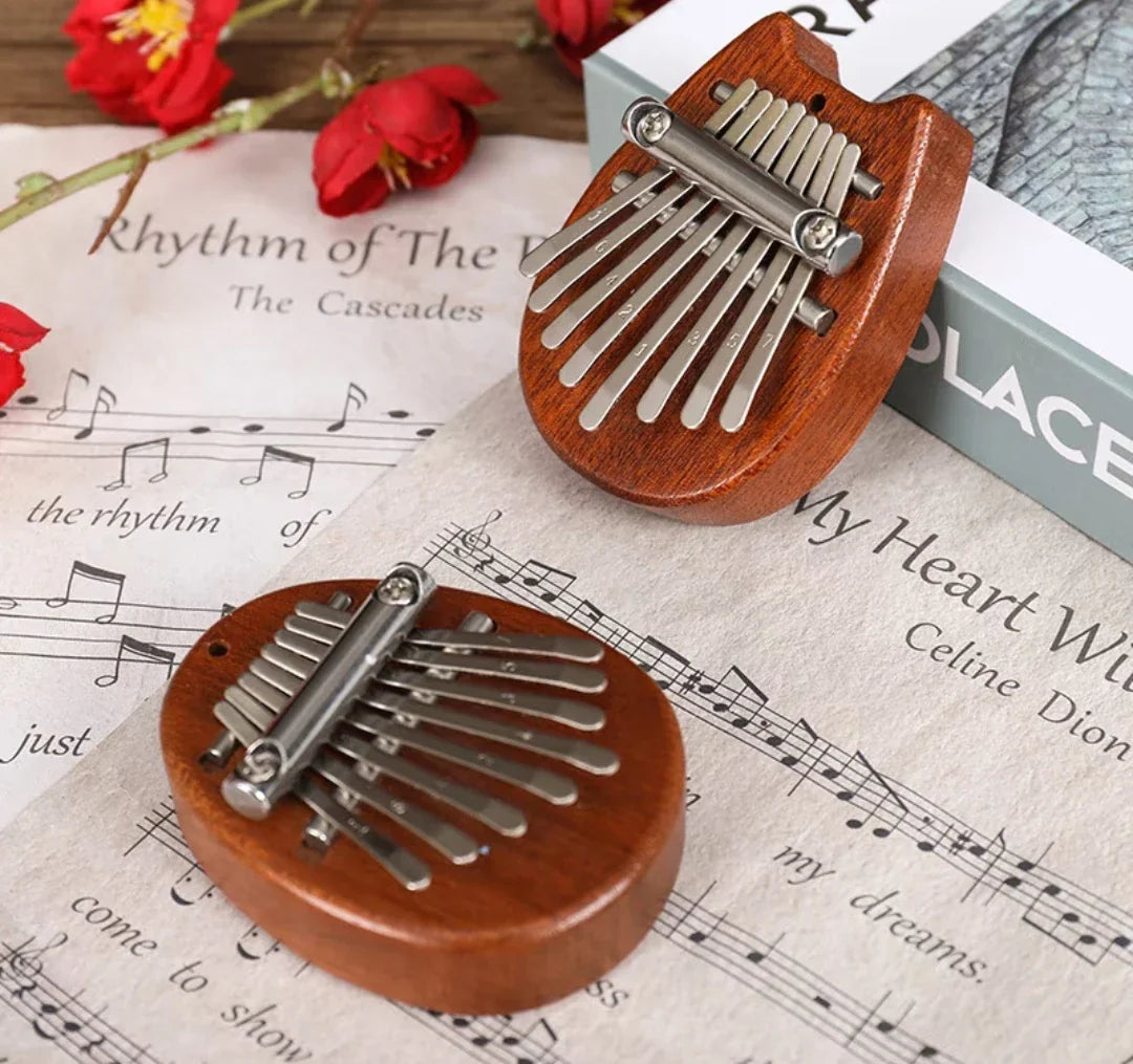 Two wooden-handled silver-keyed mini kalimba thumb pianos rest on sheet music perfect for beginners musical gift