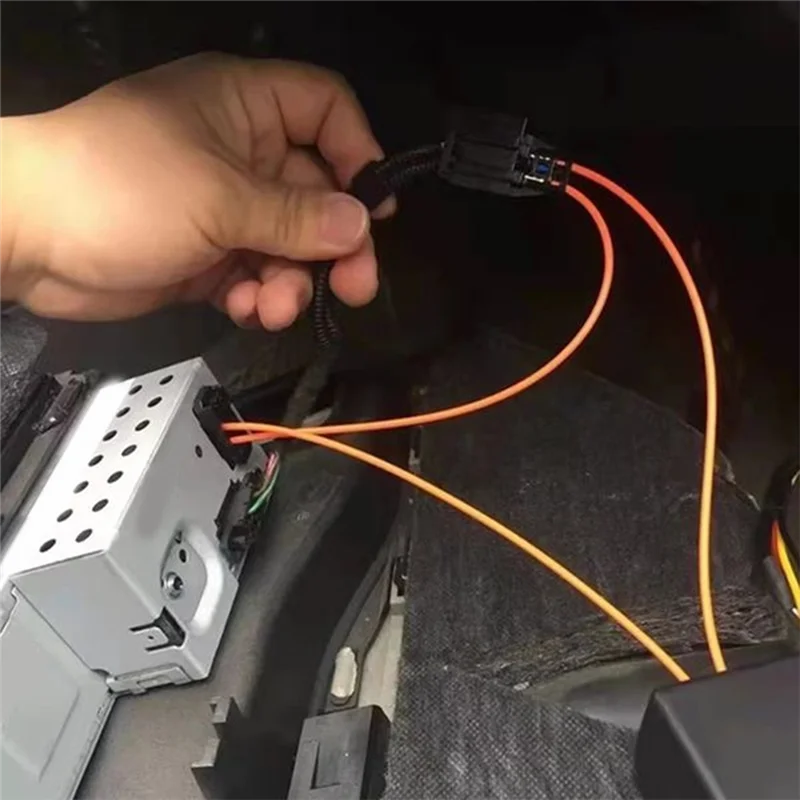 Hand holding orange wiring harness with black connectors near installed mmi 2g bluetooth music adapter car for audi a6l receiver back side