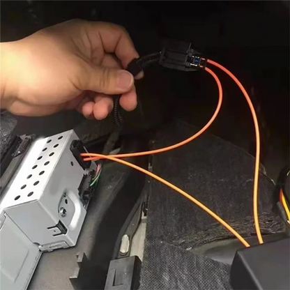 Hand holding orange wiring harness with black connectors near installed mmi 2g bluetooth music adapter car for audi a6l receiver back side