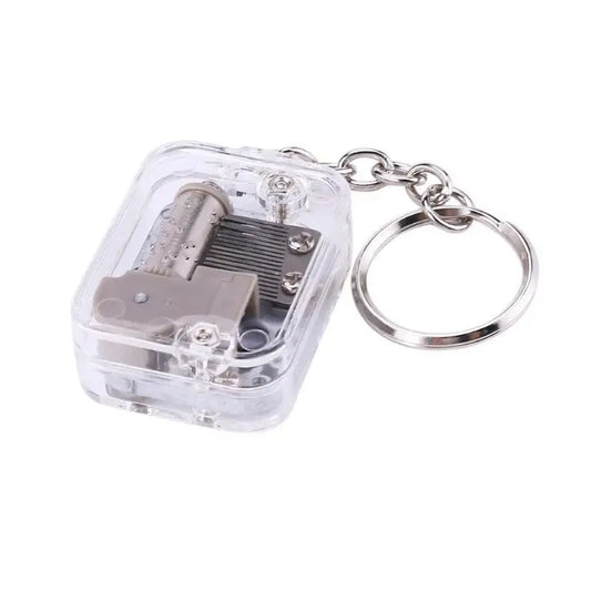 Clear plastic keychain housing a miniature silver music box movement with best mechanical metal clockwork design and screws