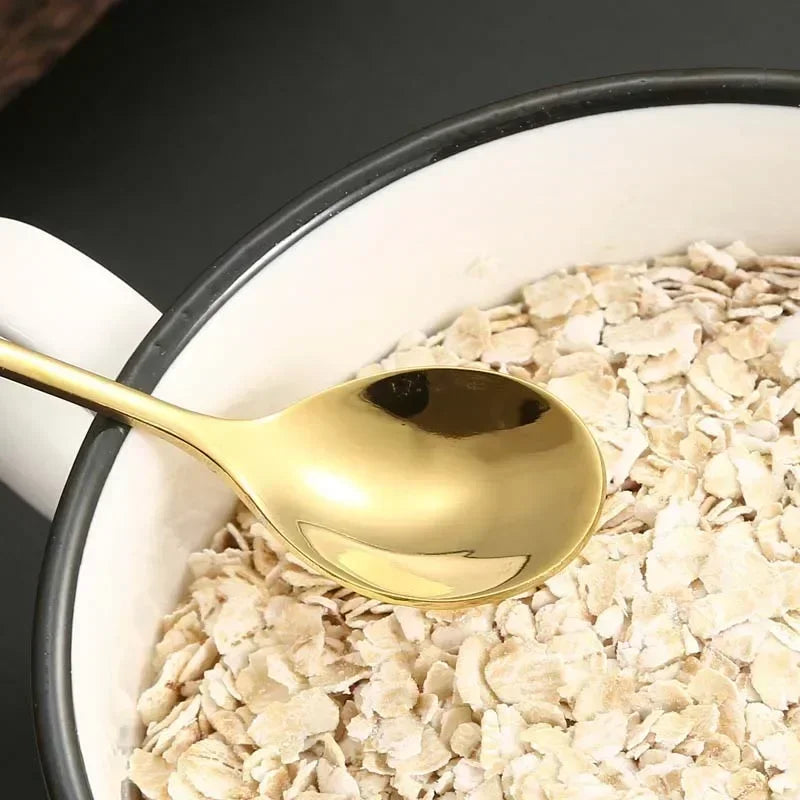 A sleek gold-colored stainless steel musical note teaspoon resting in rolled oats for mug teaspoons music use