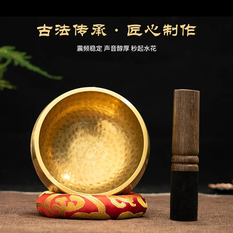 Golden hammered buddha sound bowl made of brass resting on red and gold cushion with wooden mallet for sound bowl yoga