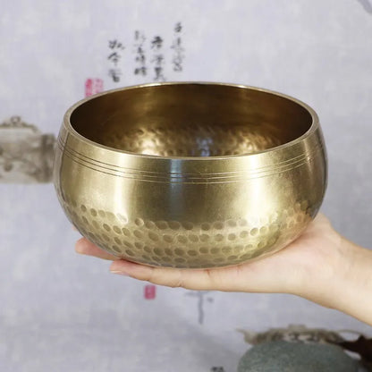 A hand holds a golden hammered brass buddha sound bowl with concentric ridges for sound bowl yoga and brass chime use