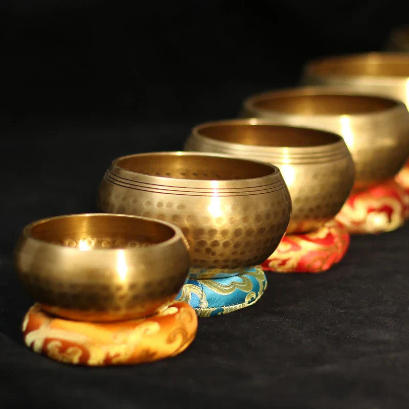 A set of golden-hued hand-hammered buddha sound bowls made of brass arranged on colorful cushions for sound bowl yoga