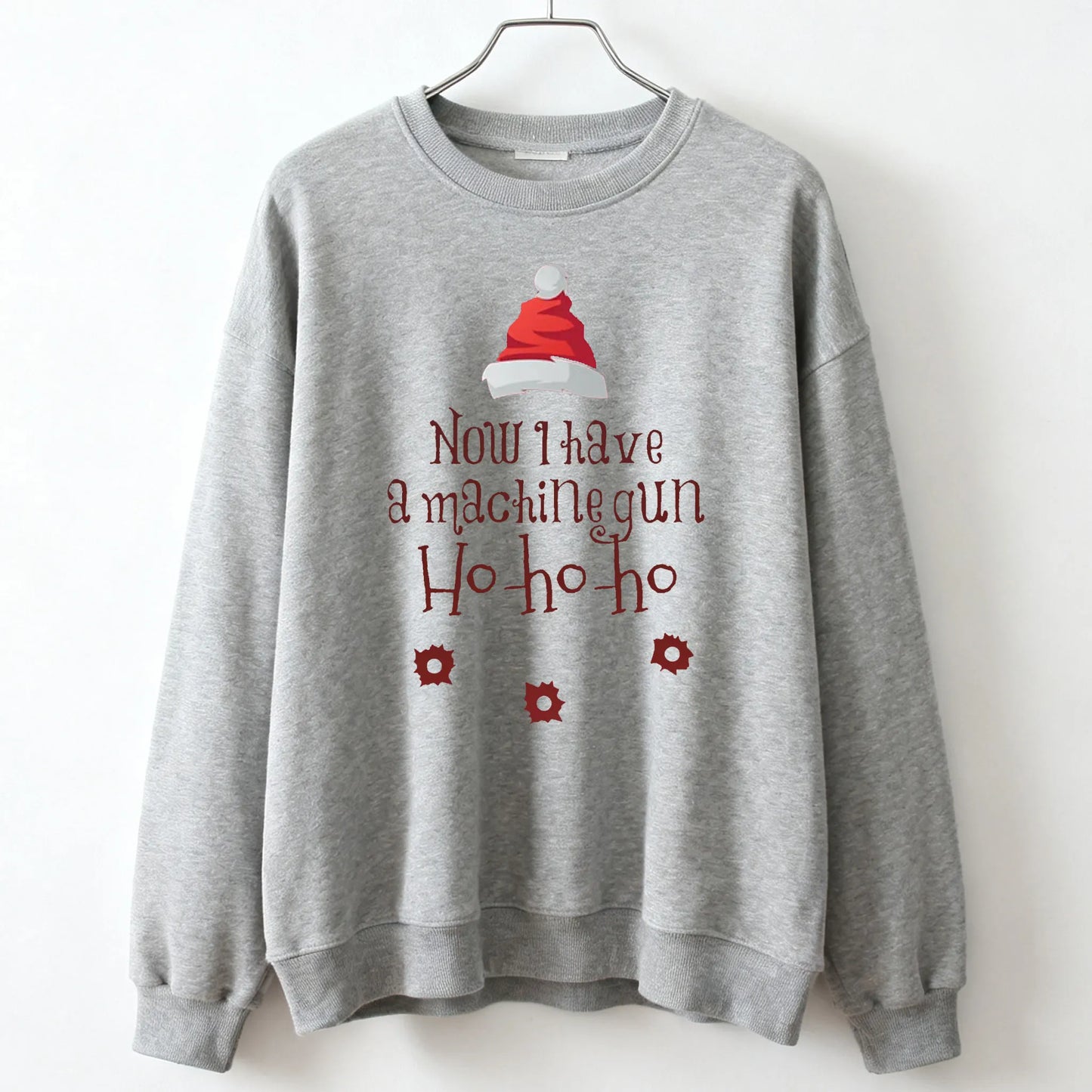 Gray crewneck sweatshirt featuring a red and white santa hat graphic with die hard mclane naktomi plaza text in maroon script